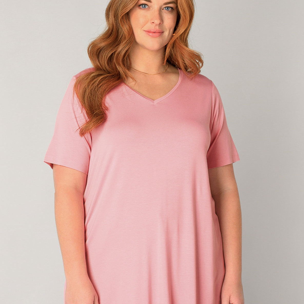 Plus Size Frau mit roten Haaren und rosafarbenem Basic-T-Shirt und hellblauer Jeans