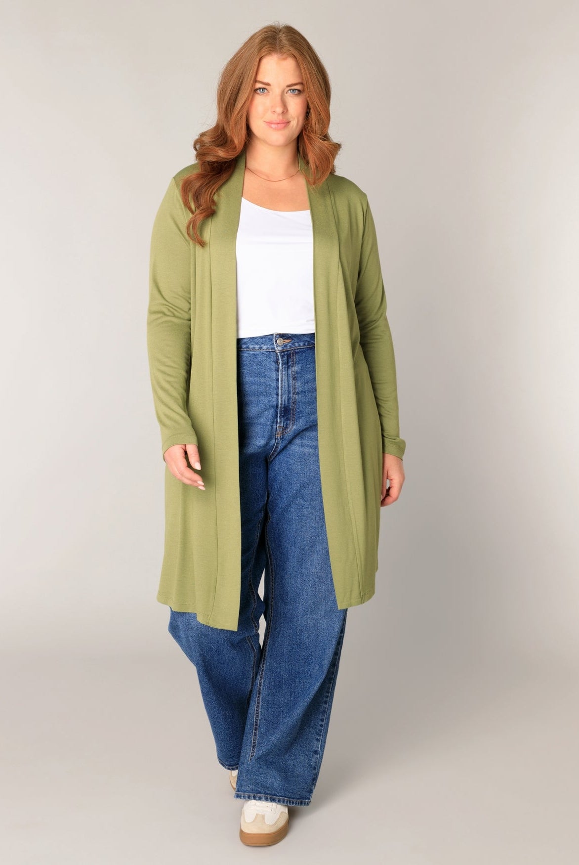 Frau mit roten Haaren, grüner Strickjacke, Jeans und weißem Top