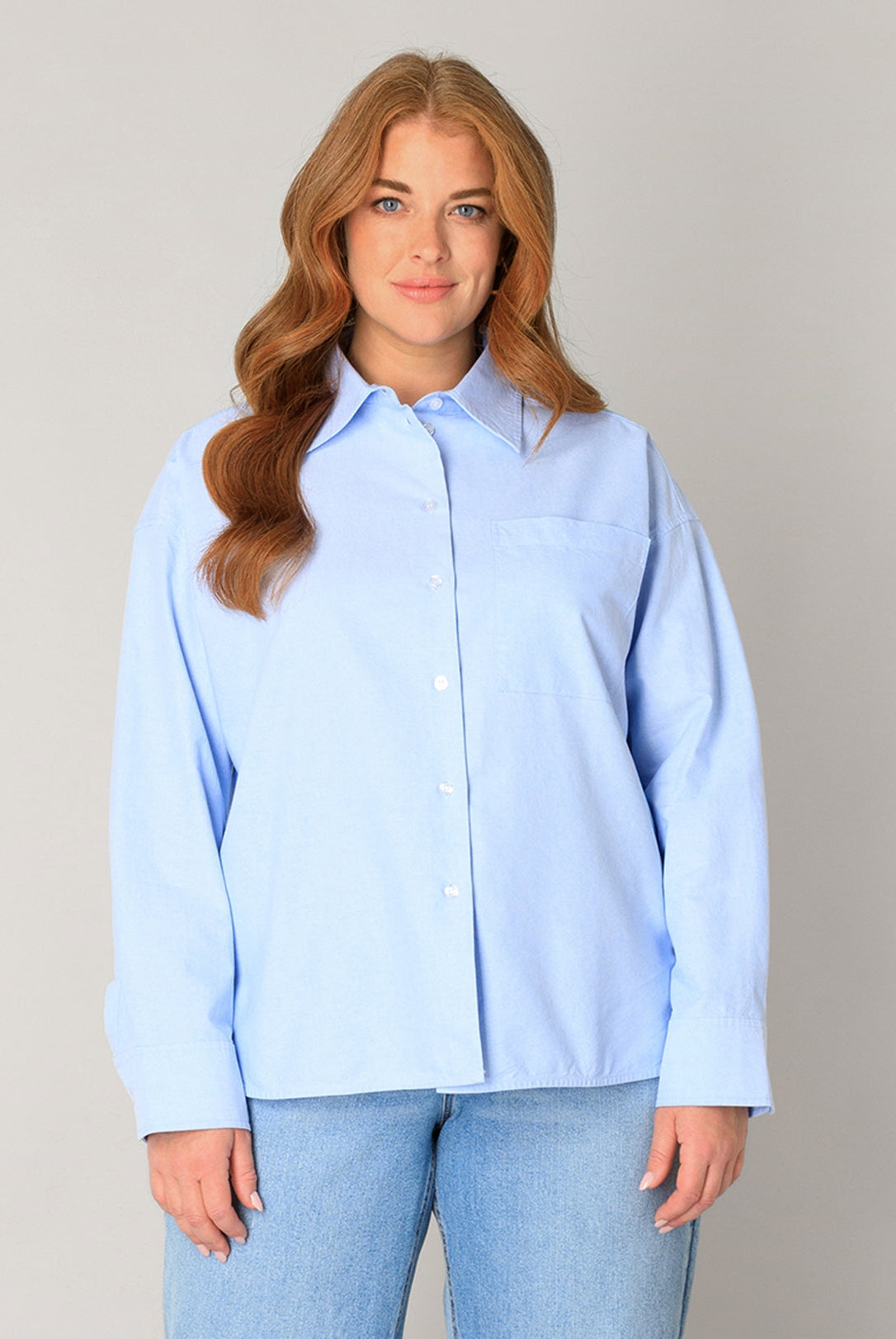 Plus Size Frau mit roten Haaren, hellblauem Blusenhemd und hellblauer Jeans