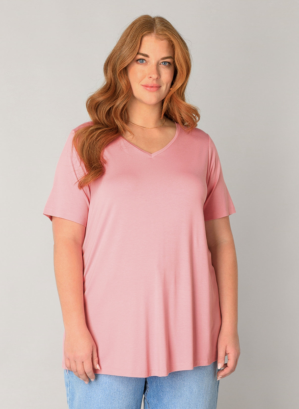 Plus Size Frau mit roten Haaren und rosafarbenem Basic-T-Shirt und hellblauer Jeans