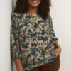 Gemusterte Plus Size Bluse mit brauner Hose an einer Frau fotografiert, die an der Wand lehnt. Marke Kaffe Curve bei Lieblingskurve kaufen